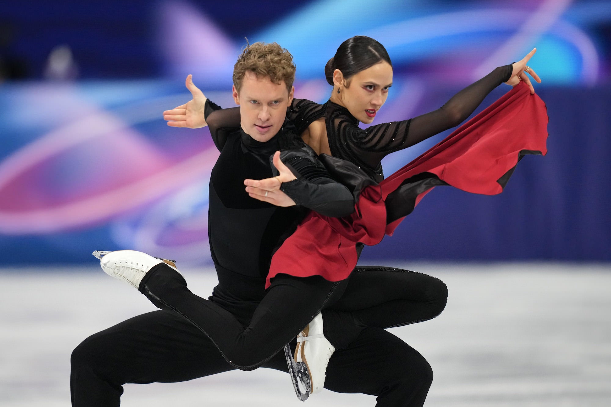 Ice dancers strike a dramatic pose in black outfits with flowing red fabric.