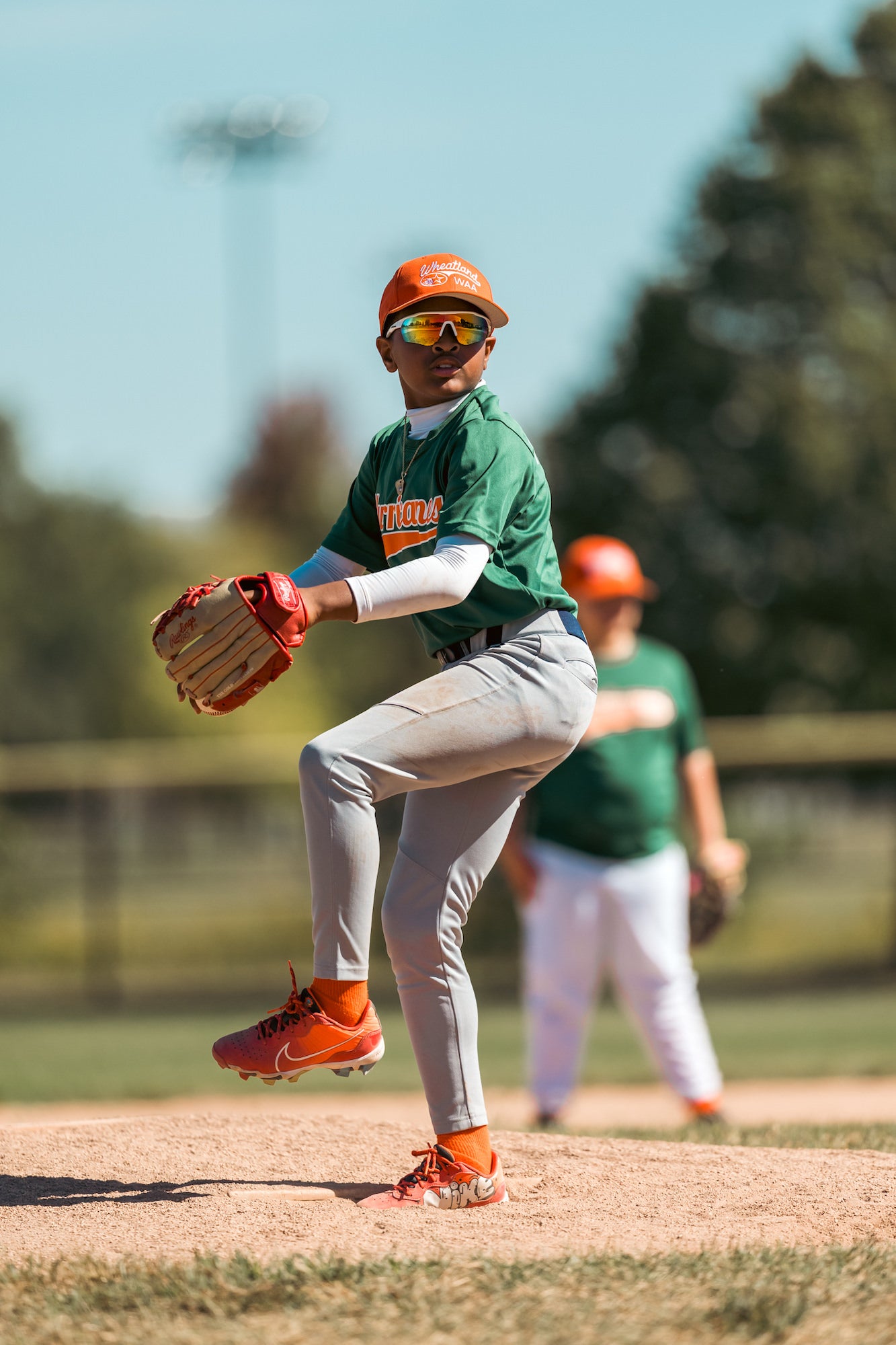 Youth pitcher at peak leg lift, set to deliver from the mound on a sunny spring day. Youth pitcher at peak leg lift, set to deliver from the mound on a sunny spring day.