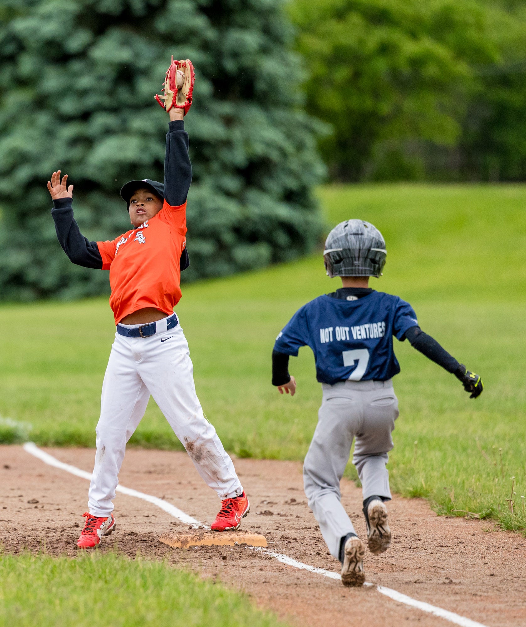 First baseman leaps to snag a high throw as a runner sprints to first on a damp infield. First baseman leaps to snag a high throw as a runner sprints to first on a damp infield.