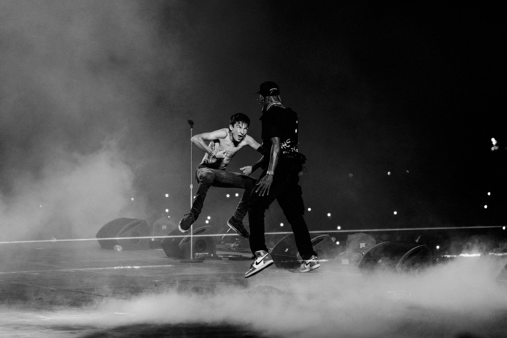 Two performers mid-jump on smoky stage, black-and-white action moment. Two performers mid-jump on smoky stage, black-and-white action moment.