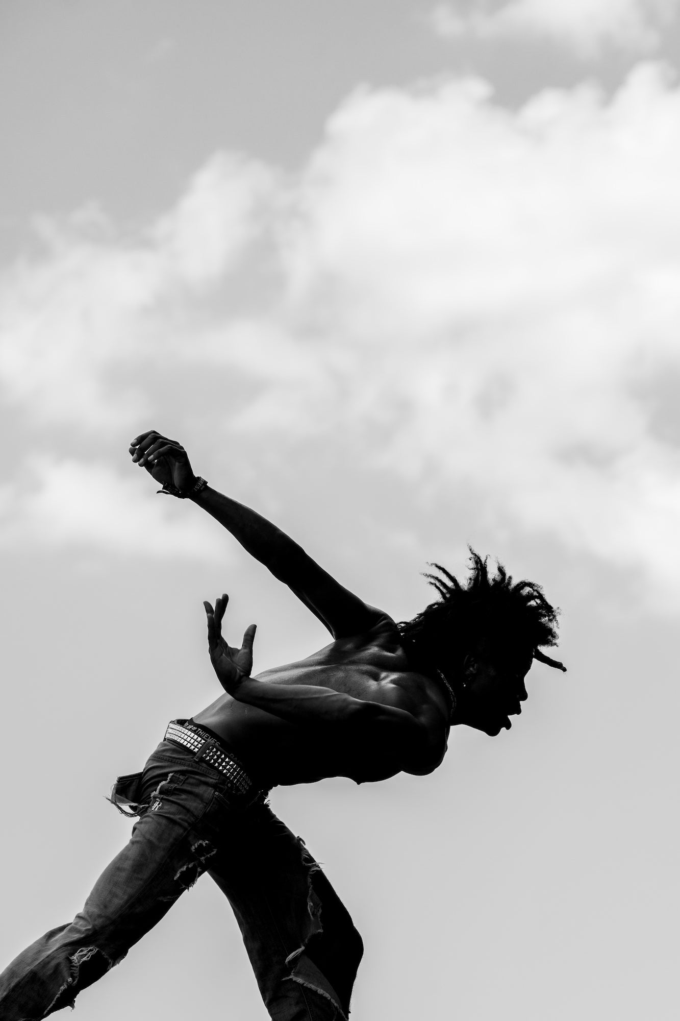 Silhouetted dancer mid-leap against cloudy sky, arms and torso arched. Silhouetted dancer mid-leap against cloudy sky, arms and torso arched.