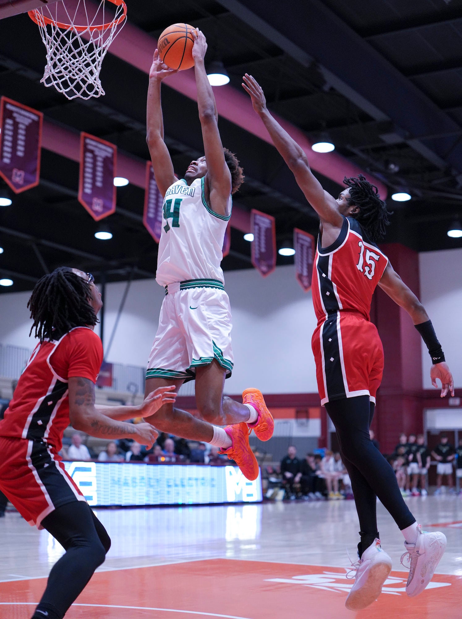 Player in white elevates for layup between two defenders under the basket