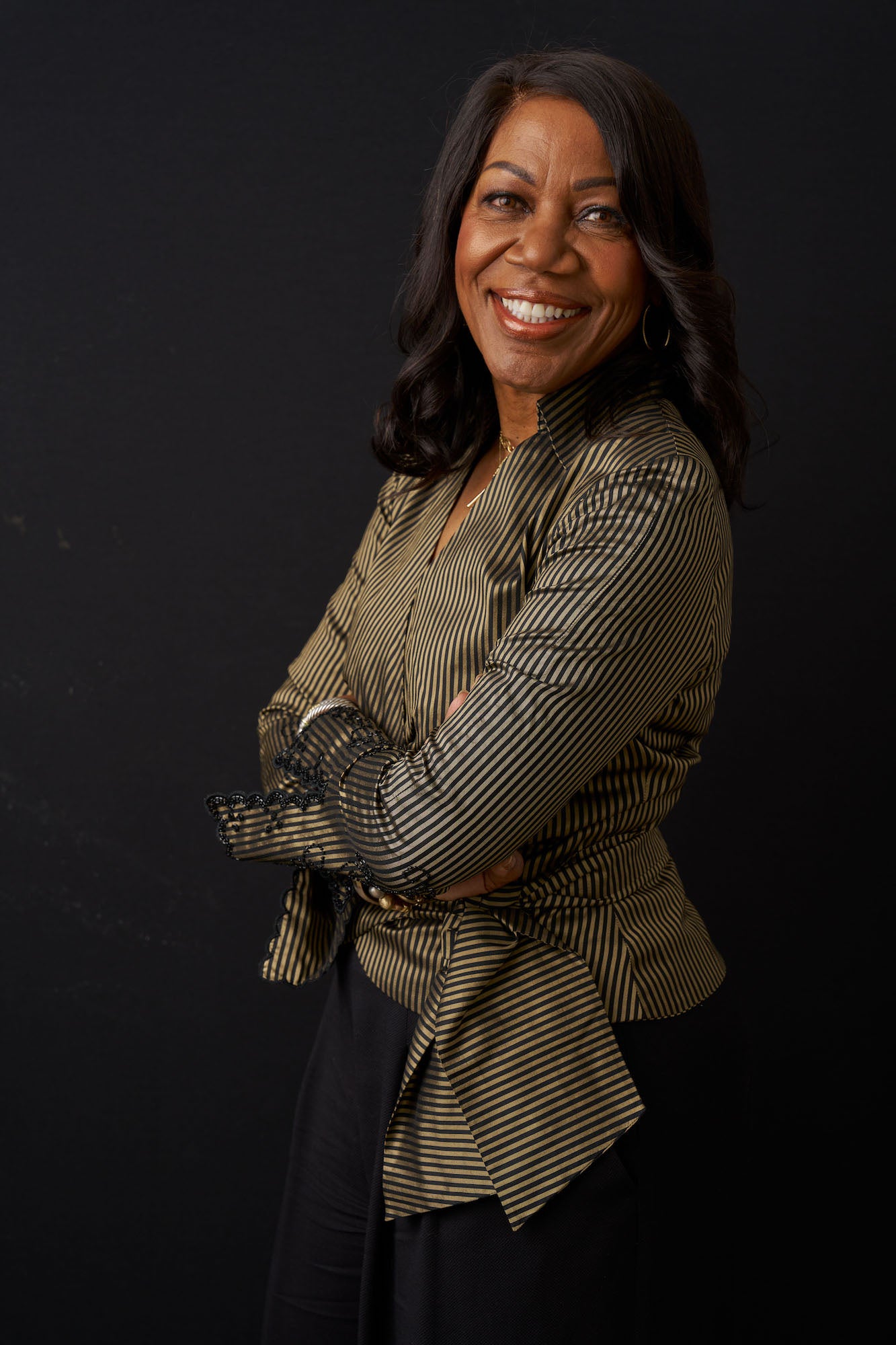 Studio portrait of a smiling woman in a striped blouse with arms crossed, black background. Studio portrait of a smiling woman in a striped blouse with arms crossed, black background.