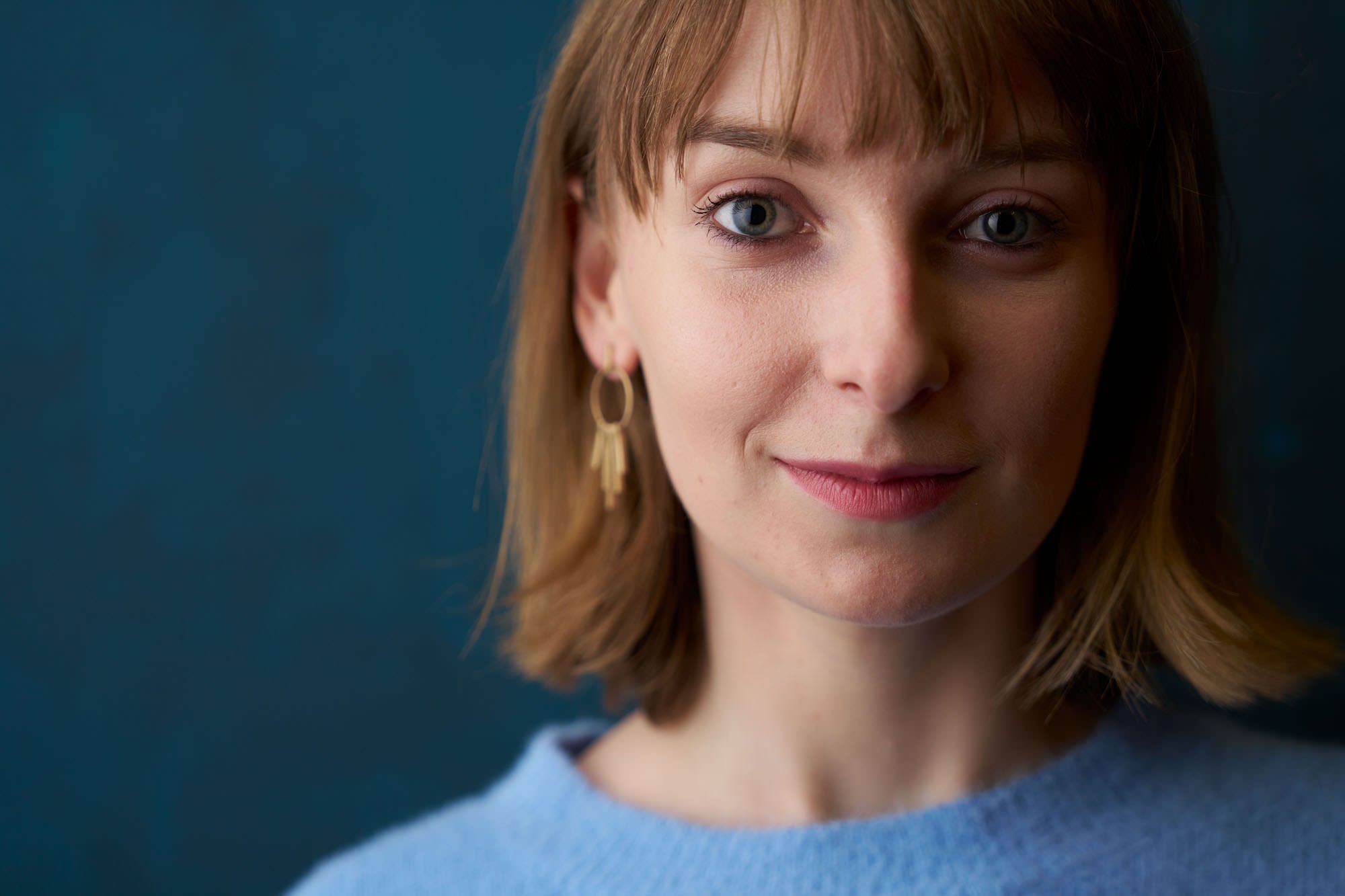 Close-up portrait of a woman in a blue sweater with gold earring, teal background and shallow depth of field. Close-up portrait of a woman in a blue sweater with gold earring, teal background and shallow depth of field.