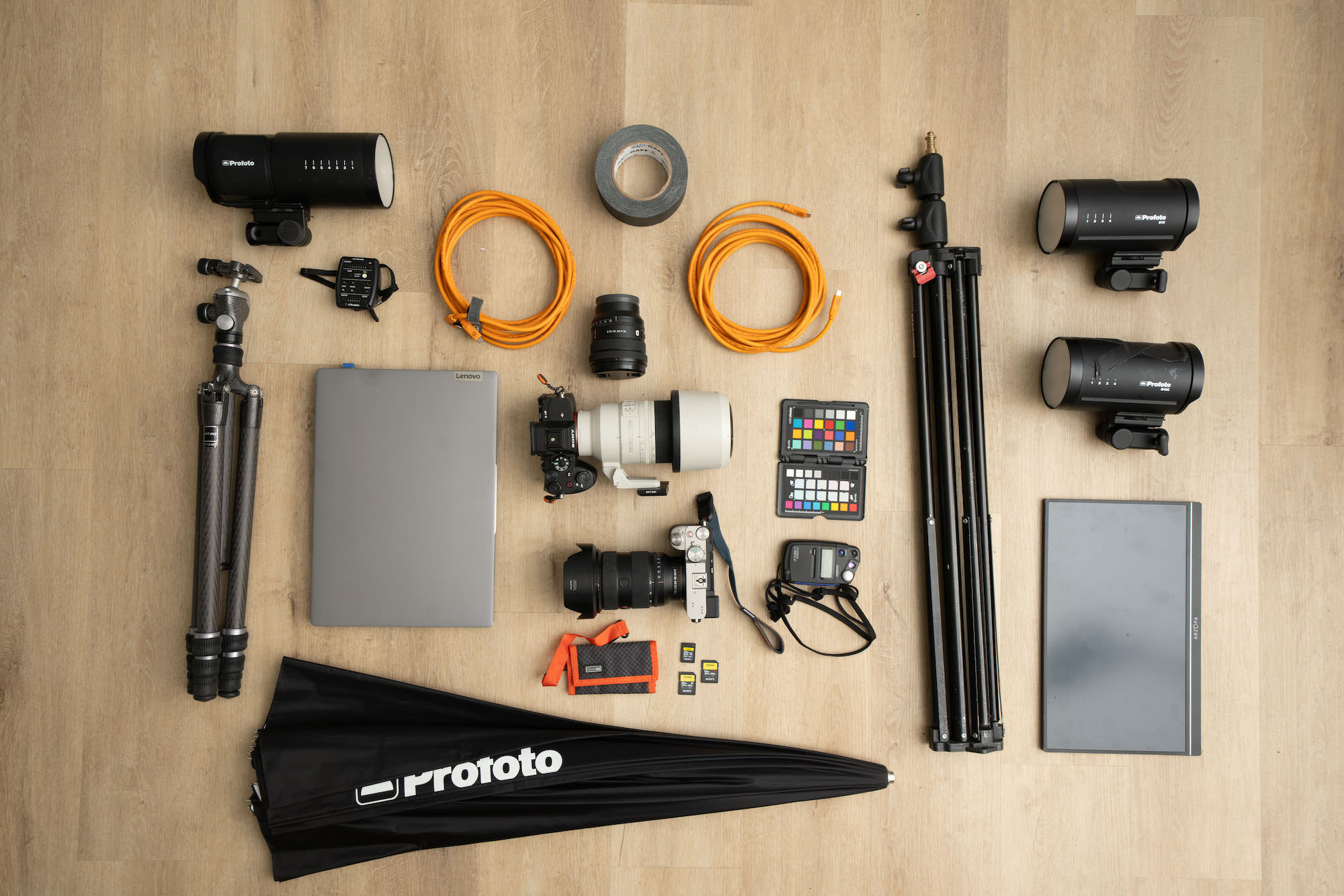 Flat lay of a headshot kit: Sony cameras and lenses, Profoto strobes, tripod, light stands, tether cables, laptop, monitor, color checker, cards, tape, and meter. Flat lay of a headshot kit: Sony cameras and lenses, Profoto strobes, tripod, light stands, tether cables, laptop, monitor, color checker, cards, tape, and meter.