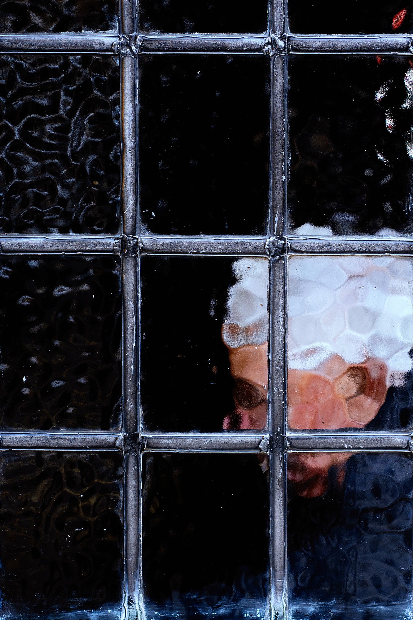 Obscured face framed by textured window panes, dark moody portrait. Obscured face framed by textured window panes, dark moody portrait.