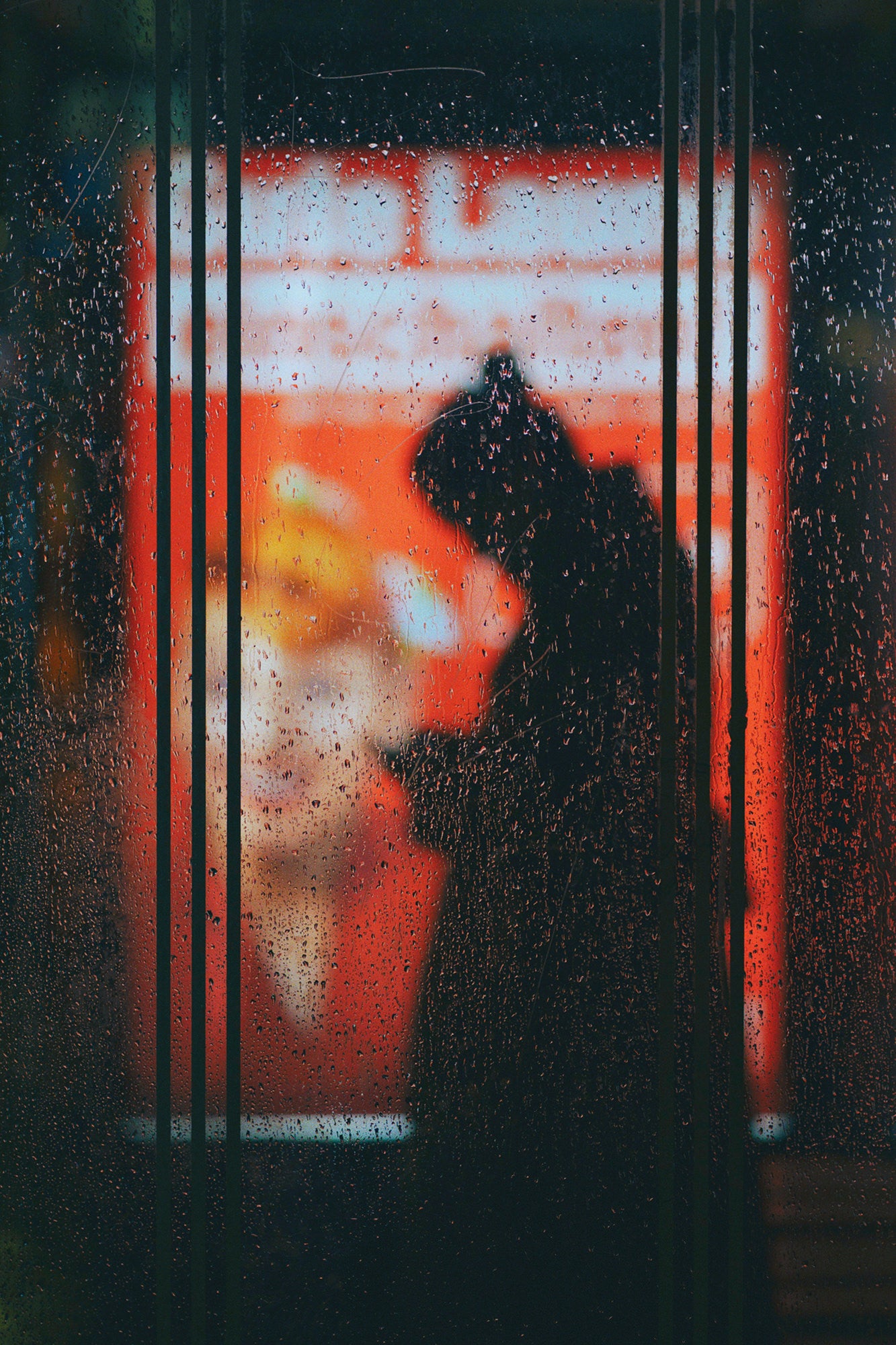 Silhouette at a rainy bus stop seen through wet glass and orange signage. Silhouette at a rainy bus stop seen through wet glass and orange signage.